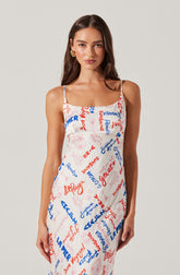 A woman is wearing a sleeveless, spaghetti strap dress with a white background. The dress is decorated with various colorful text and graphic elements in red and blue, including words like "Gelato," "Summer," and "Vitamin." The overall style of the dress is casual and summery.